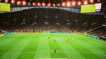 A packed football stadium during a match, featuring teams in white and red kits under bright stadium lights