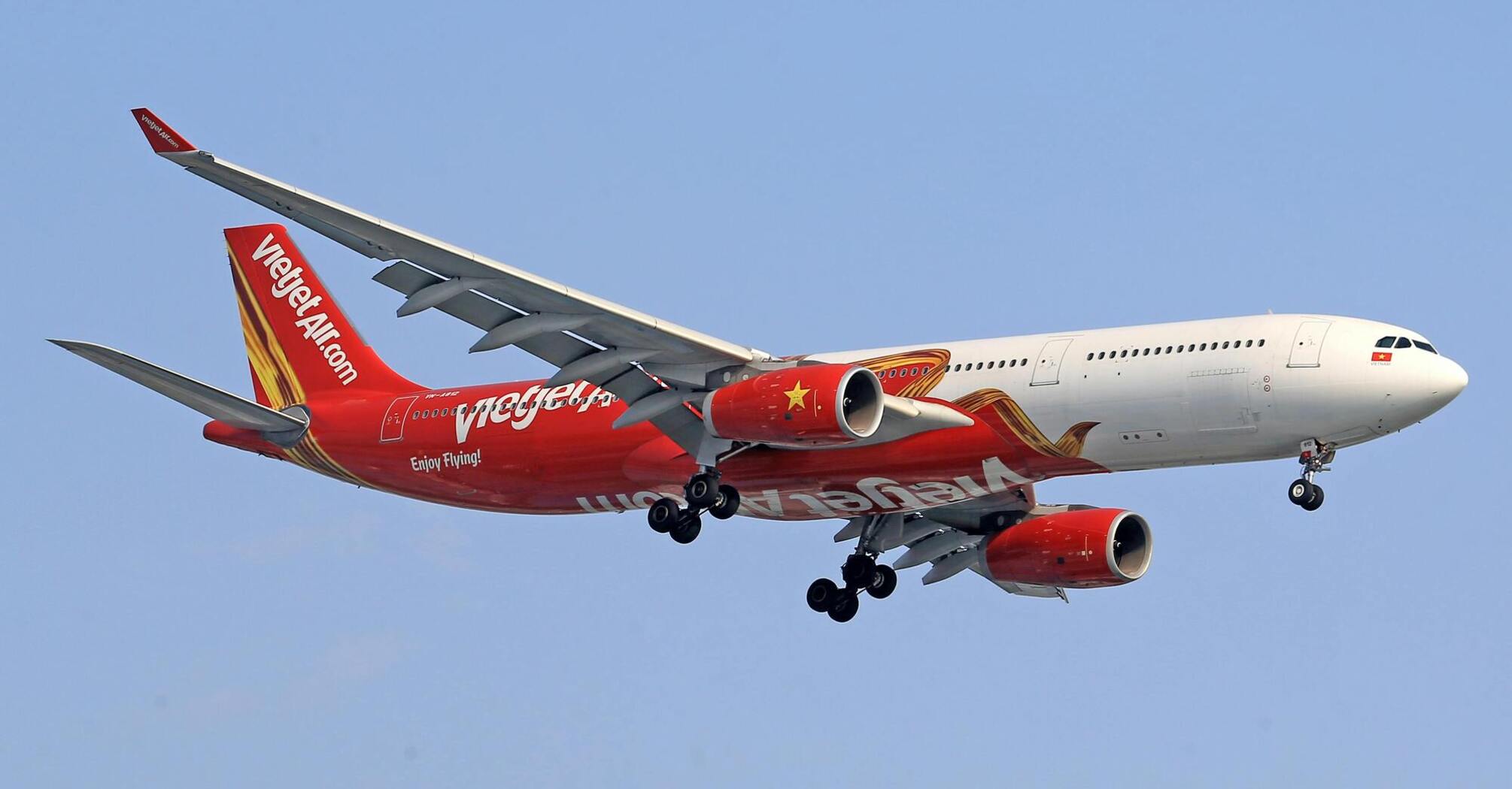 A Vietjet aircraft in flight against a clear blue sky, showcasing the airline's red and white livery