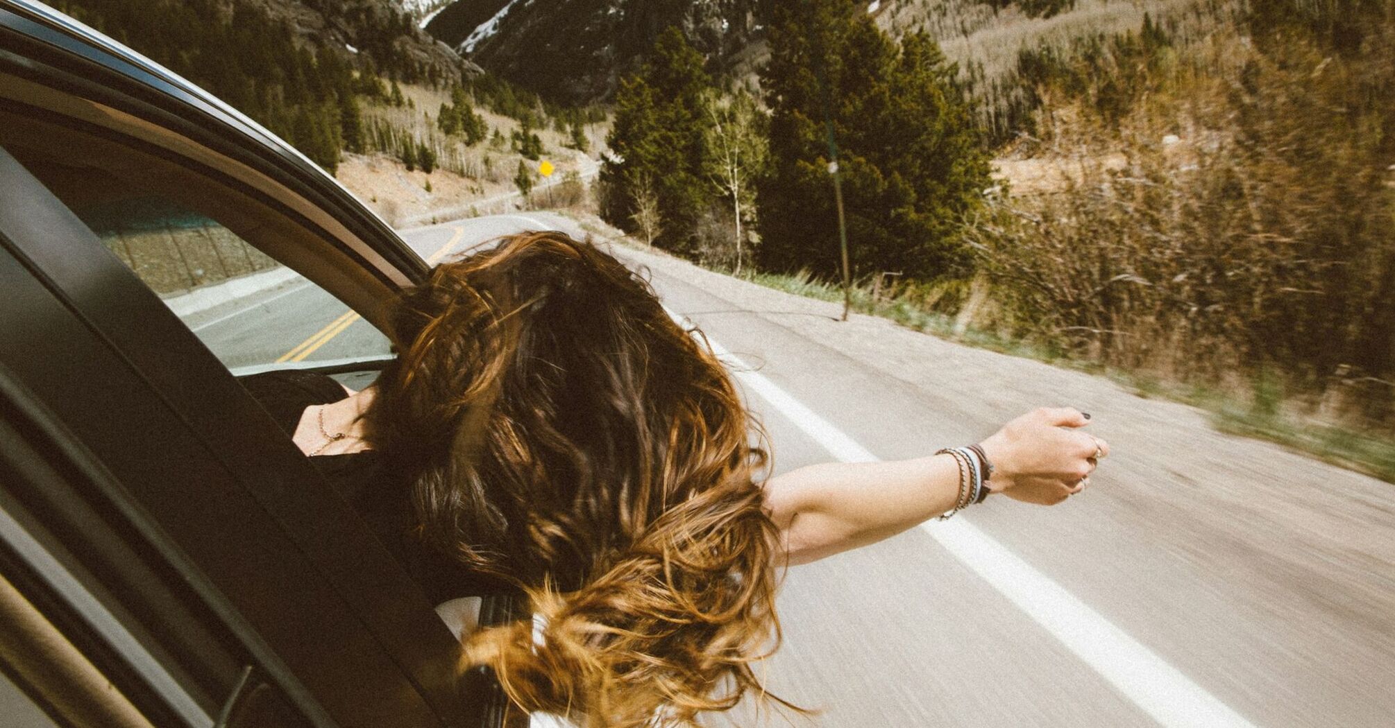 Person leaning out of a car window on a mountain road, enjoying the fresh air and scenic view