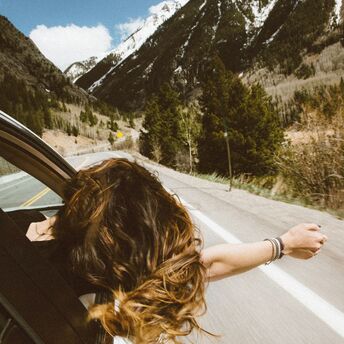 Person leaning out of a car window on a mountain road, enjoying the fresh air and scenic view