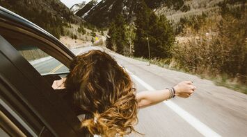 Person leaning out of a car window on a mountain road, enjoying the fresh air and scenic view