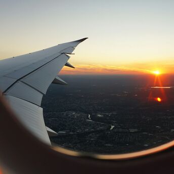 A view of a sunset from an airplane window, showing the aircraft's wing and a city below