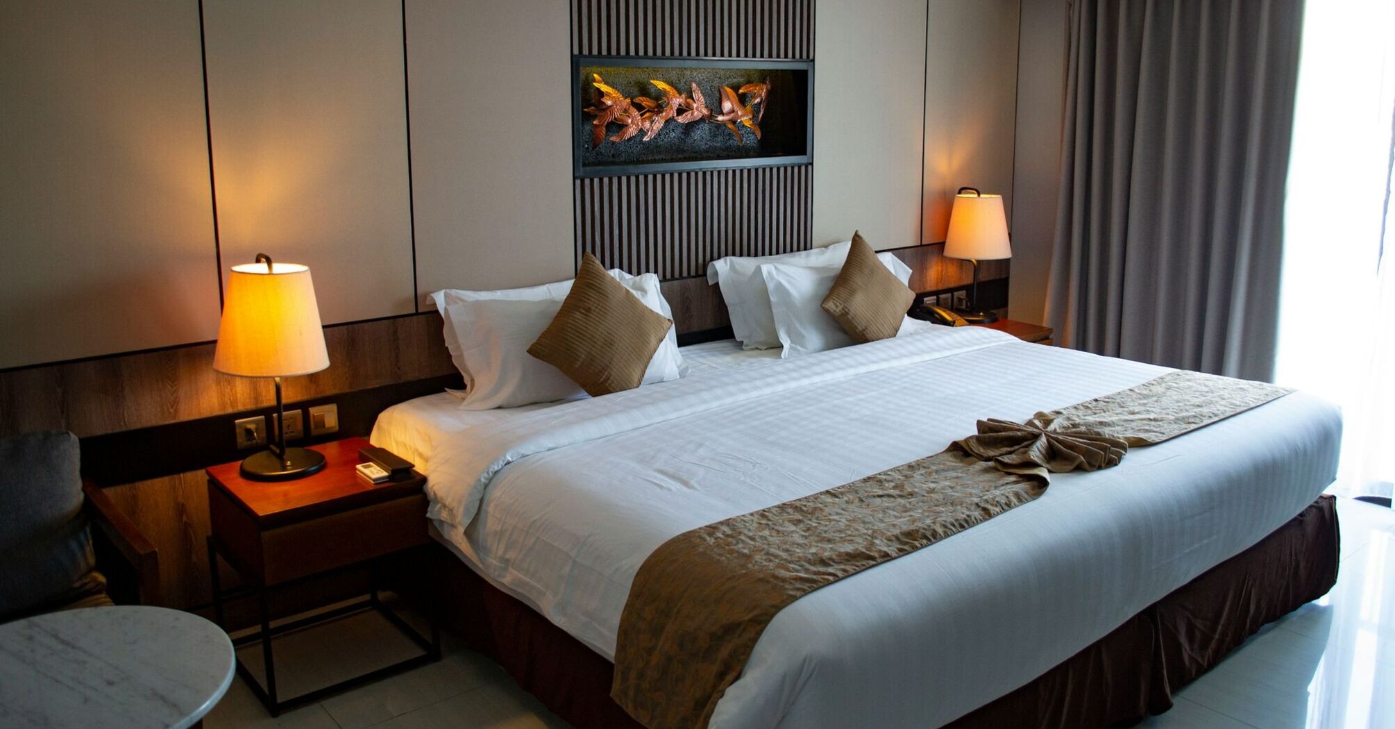 A modern hotel room with a neatly made king-sized bed, soft lighting from bedside lamps, and elegant wall decor