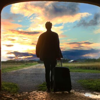 A traveler with a suitcase walking towards a scenic sunset, symbolizing exploration and new adventures