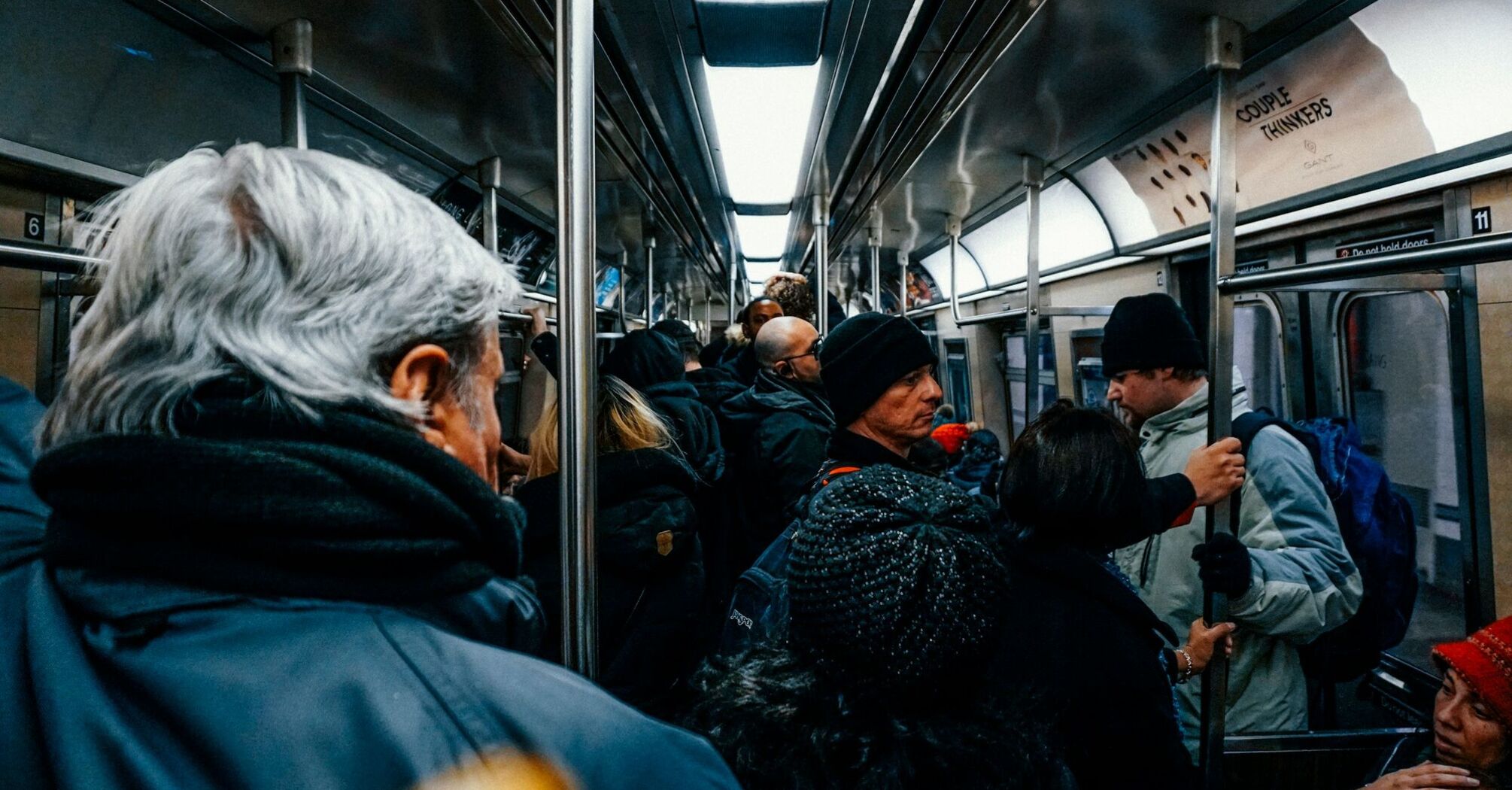 A crowded subway train with passengers wearing winter clothing, holding onto handrails and standing close together