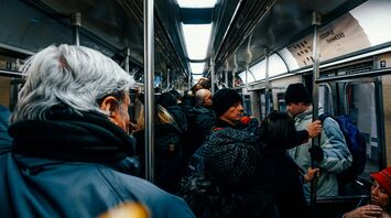 A crowded subway train with passengers wearing winter clothing, holding onto handrails and standing close together