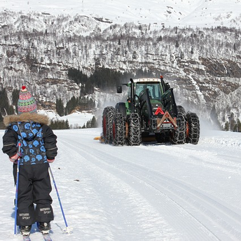 A child skiing towards a large snow tractor with six wheels, wrapped in chains for snow navigation