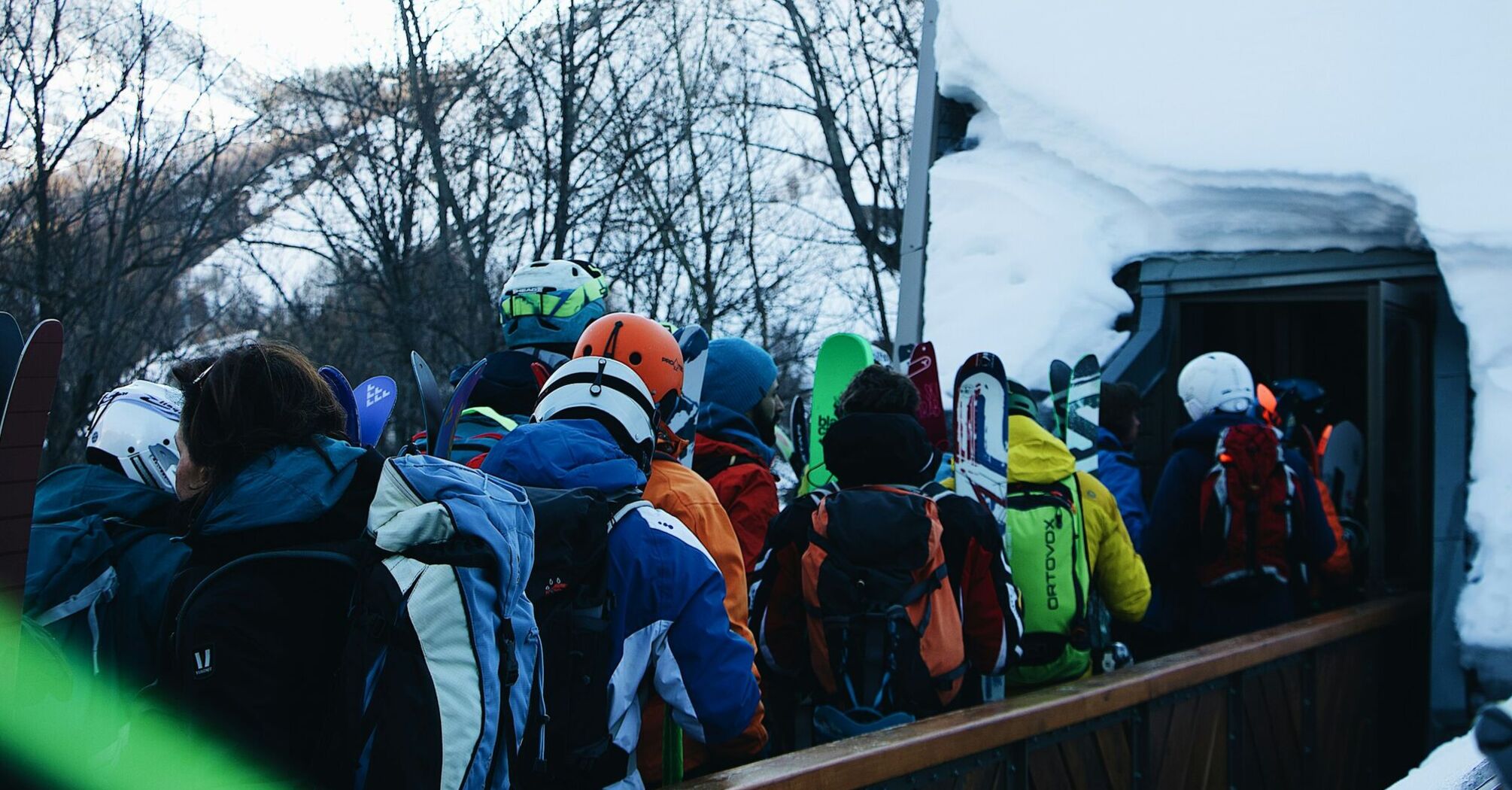 A crowd of skiers with colorful gear waiting in line at a snow-covered ski resort entrance