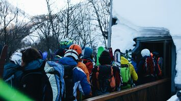 A crowd of skiers with colorful gear waiting in line at a snow-covered ski resort entrance