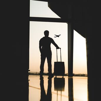 A silhouette of a traveler with a suitcase at an airport, watching a plane take off against the sunset