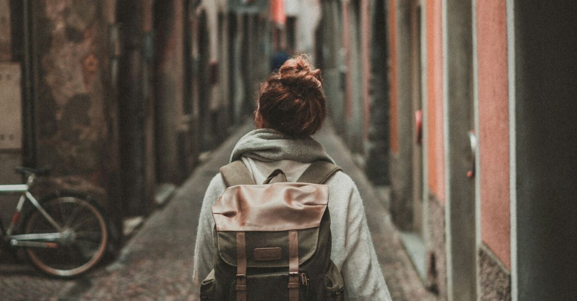 A solo traveler with a backpack walking through a narrow cobblestone street in an old European town