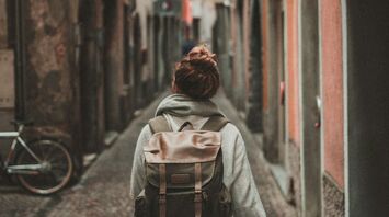 A solo traveler with a backpack walking through a narrow cobblestone street in an old European town
