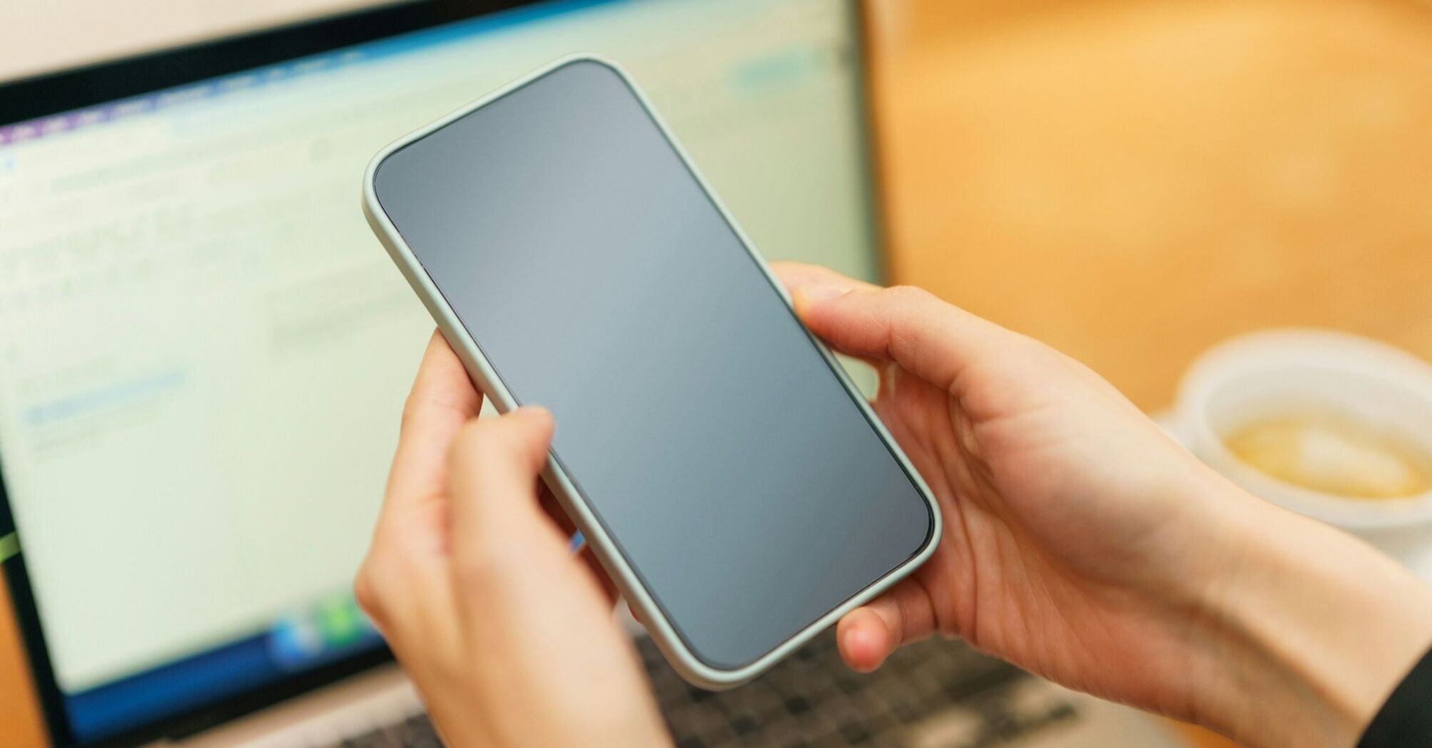 A person holding a smartphone in front of a laptop screen, symbolizing digital connectivity and modern payment solutions