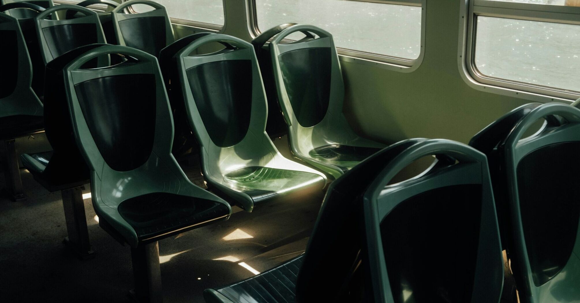 Empty green seats inside a public transport vehicle illuminated by sunlight through the windows