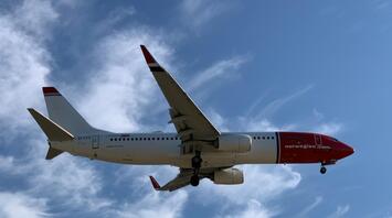 Norwegian aircraft approaching for landing under clear blue sky