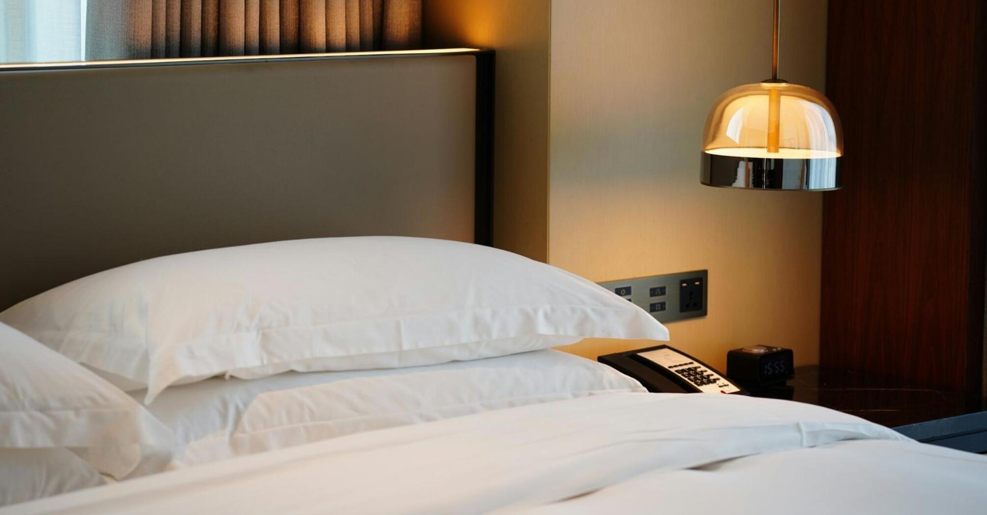 Neatly made hotel bed with white pillows and bedside lamp