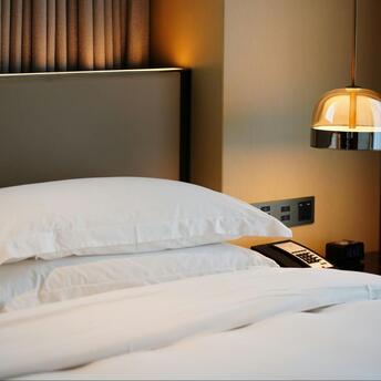 Neatly made hotel bed with white pillows and bedside lamp