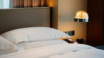 Neatly made hotel bed with white pillows and bedside lamp