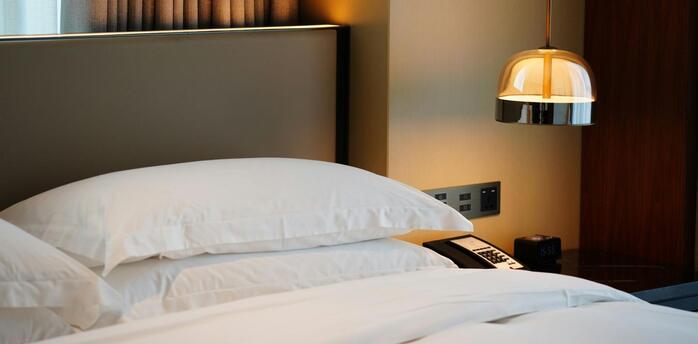 Neatly made hotel bed with white pillows and bedside lamp