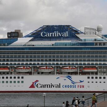 Carnival cruise ship docked at a port with passengers walking nearby