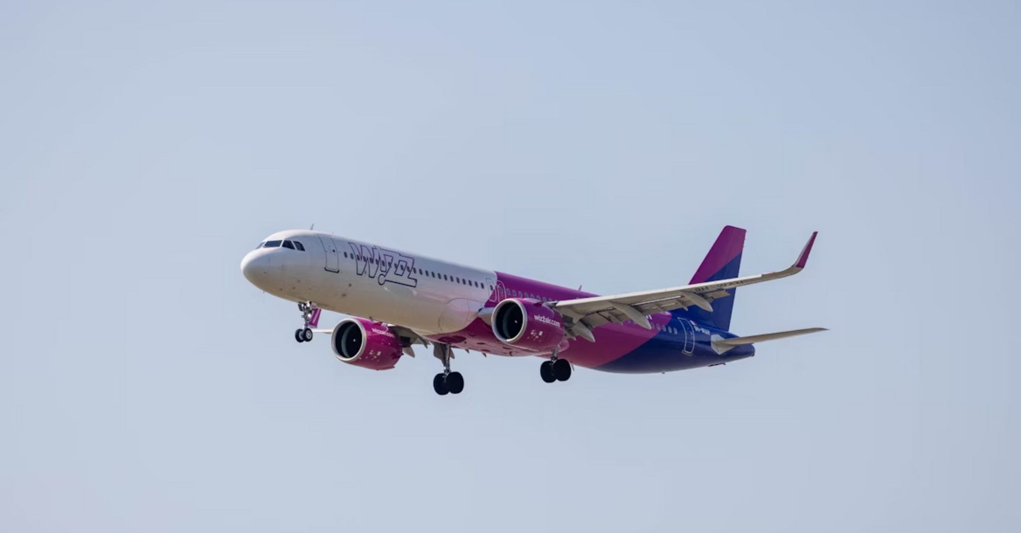 A Wizz Air aircraft approaching for landing against a clear sky
