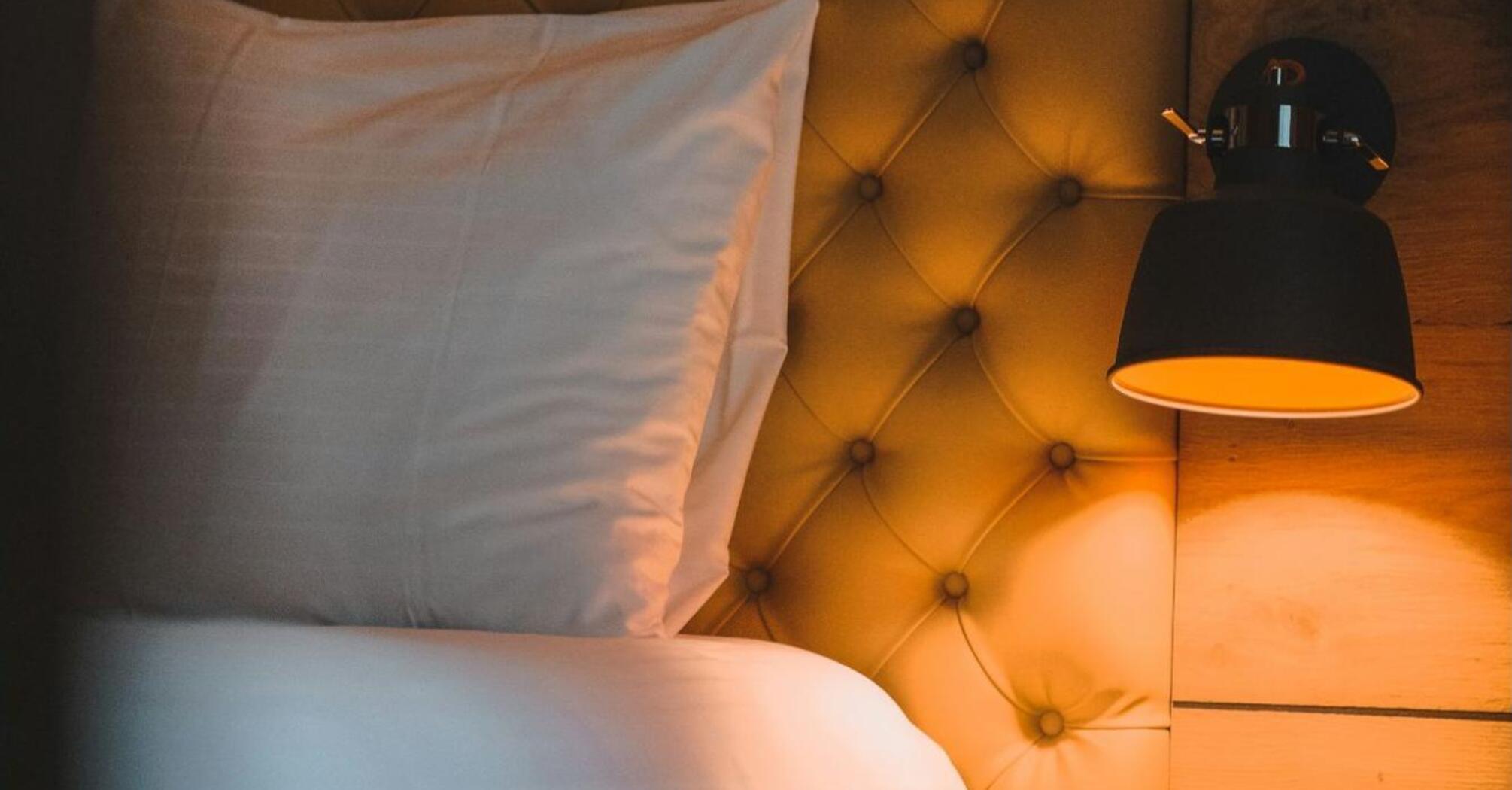 Softly lit hotel bed with tufted headboard and night lamp