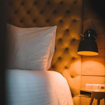 Softly lit hotel bed with tufted headboard and night lamp