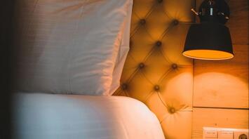 Softly lit hotel bed with tufted headboard and night lamp