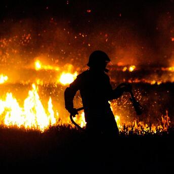 Firefighter battling massive flames during a nighttime wildfire