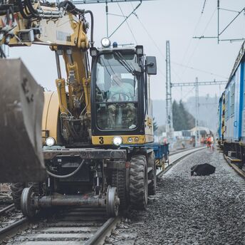 Construction machinery working on railway tracks during maintenance near a passenger train