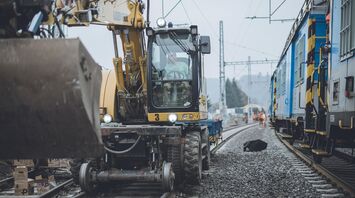 Construction machinery working on railway tracks during maintenance near a passenger train