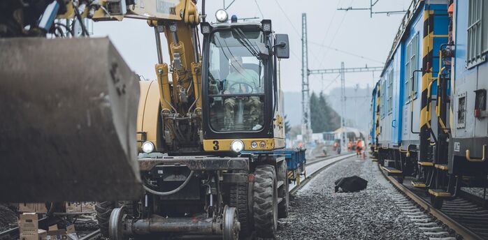 Construction machinery working on railway tracks during maintenance near a passenger train