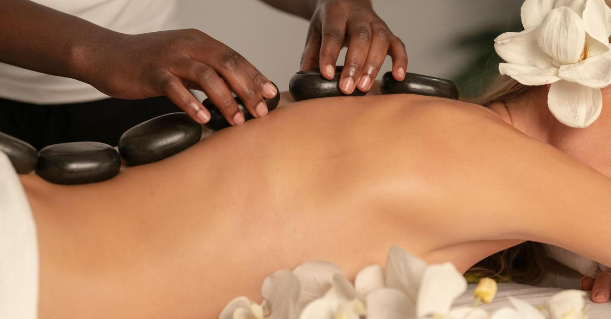 A person receiving a hot stone massage with white orchids nearby