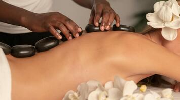 A person receiving a hot stone massage with white orchids nearby