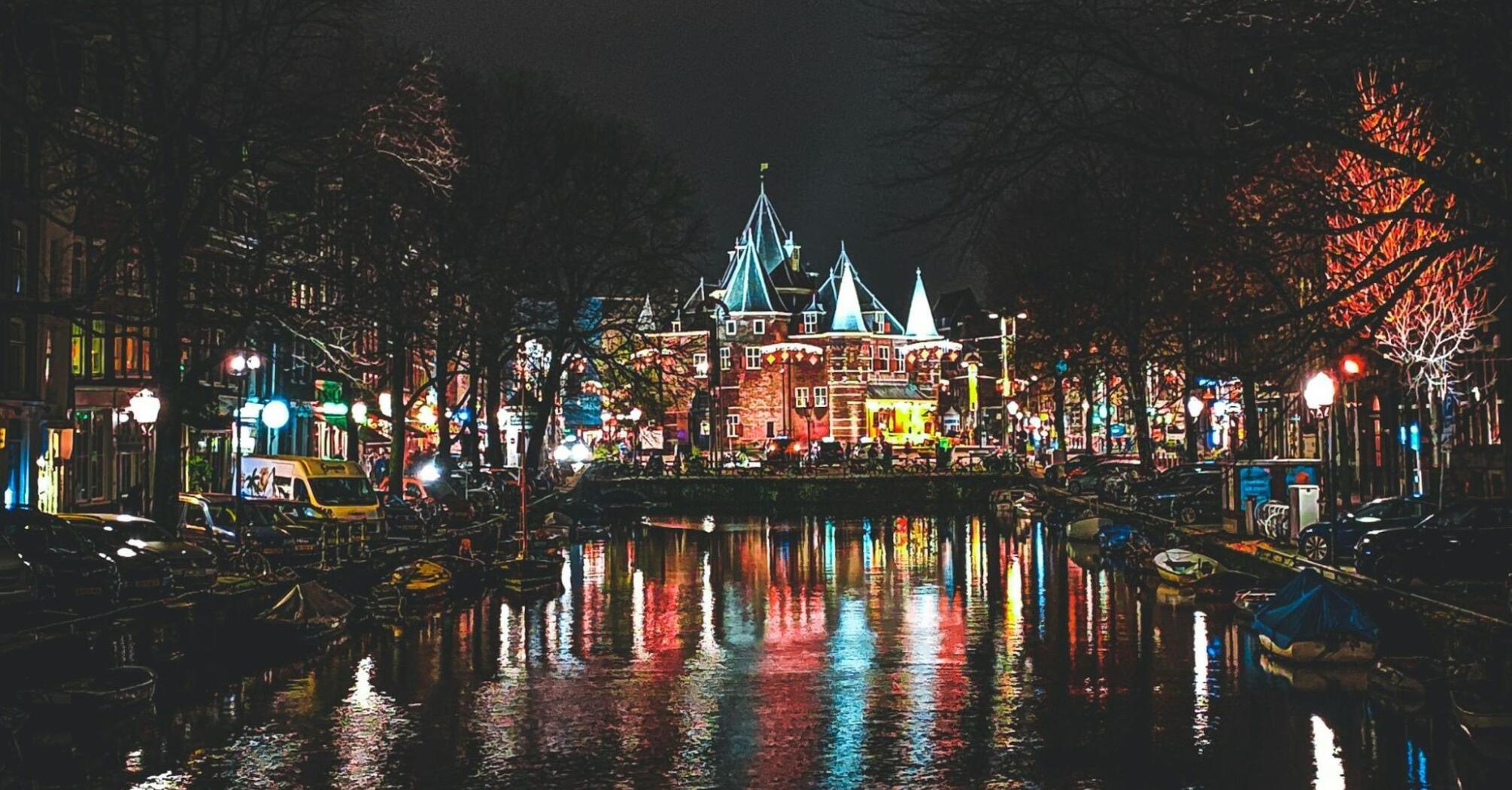 Night view of Amsterdam’s canals reflecting colorful city lights near the historic Waag building