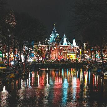 Night view of Amsterdam’s canals reflecting colorful city lights near the historic Waag building