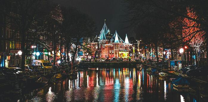 Night view of Amsterdam’s canals reflecting colorful city lights near the historic Waag building