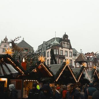 Crowds gather at decorated wooden stalls during a festive winter market in a European town square