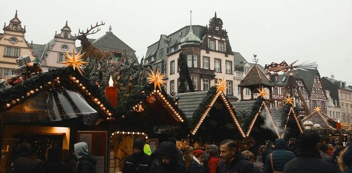 Crowds gather at decorated wooden stalls during a festive winter market in a European town square