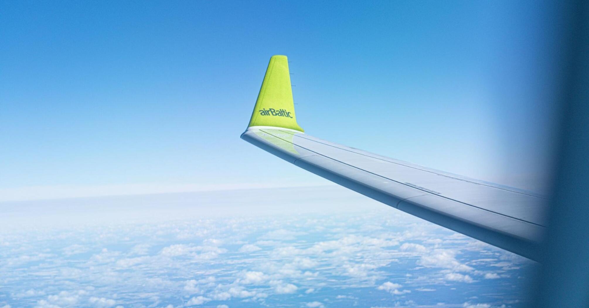 airBaltic aircraft wing flying above the clouds on a clear day