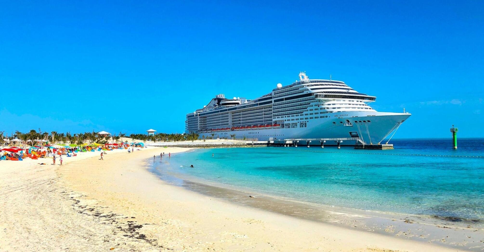 Cruise ship docked near a tropical beach with clear blue water