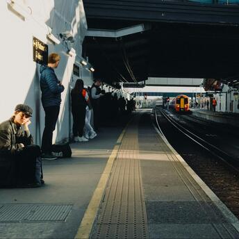 Passengers waiting at a train station platform in sunlight as a train approaches
