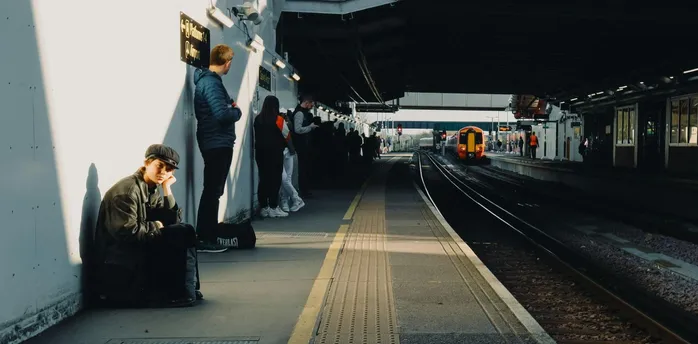 Passengers waiting at a train station platform in sunlight as a train approaches