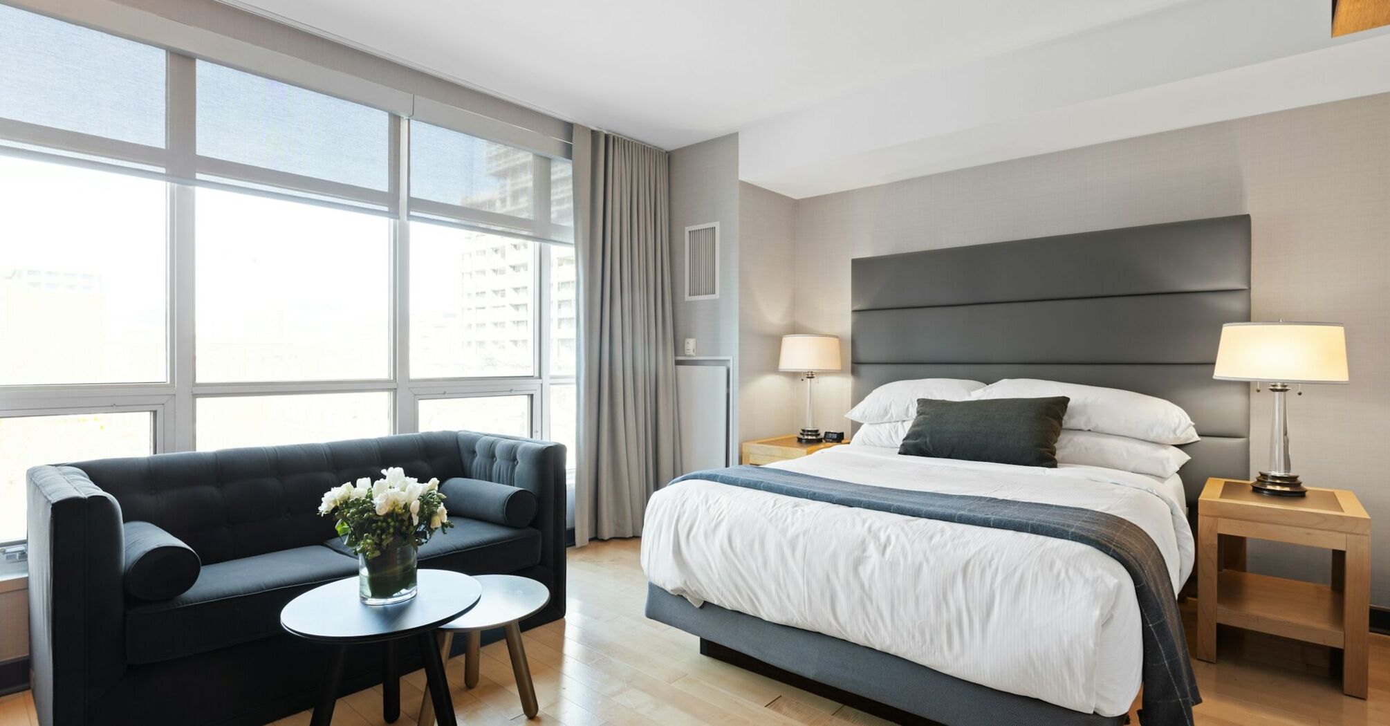 Modern hotel room with large windows, a king-size bed, and a seating area