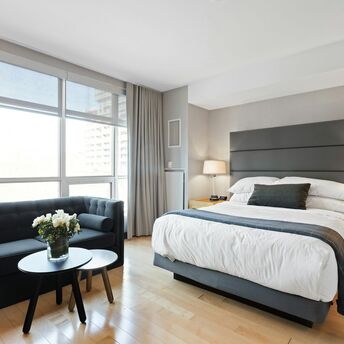 Modern hotel room with large windows, a king-size bed, and a seating area