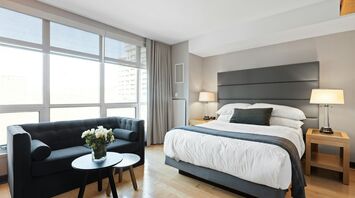 Modern hotel room with large windows, a king-size bed, and a seating area