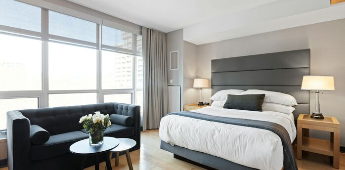 Modern hotel room with large windows, a king-size bed, and a seating area