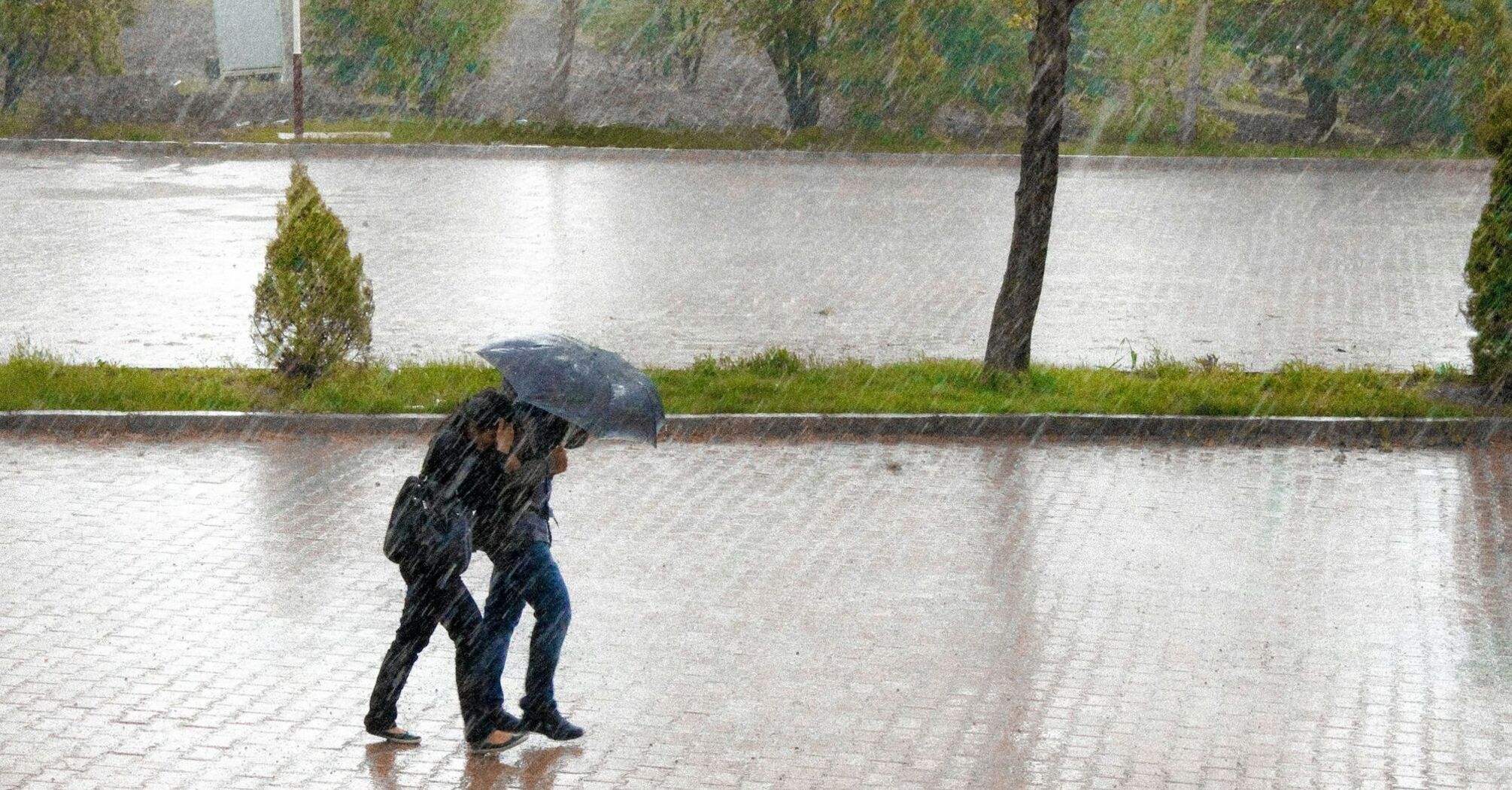 Two travelers walking under heavy rain with an umbrella