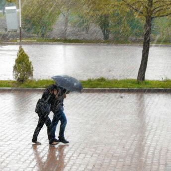 Two travelers walking under heavy rain with an umbrella