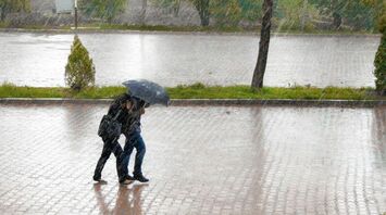 Two travelers walking under heavy rain with an umbrella